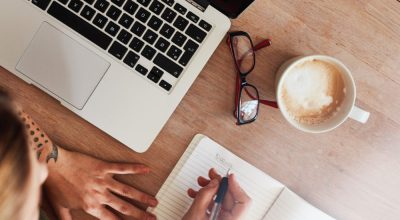 Top view shot of woman sitting at table with laptop and coffee writing on notebook. Female making to do list on diary.